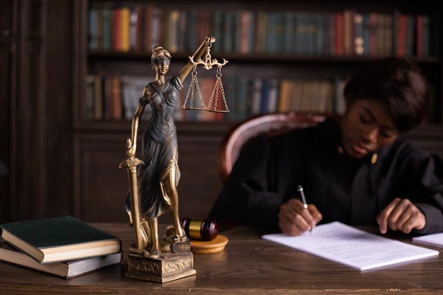 a judge signing a document while sat at a desk with a lady of justice statue on it