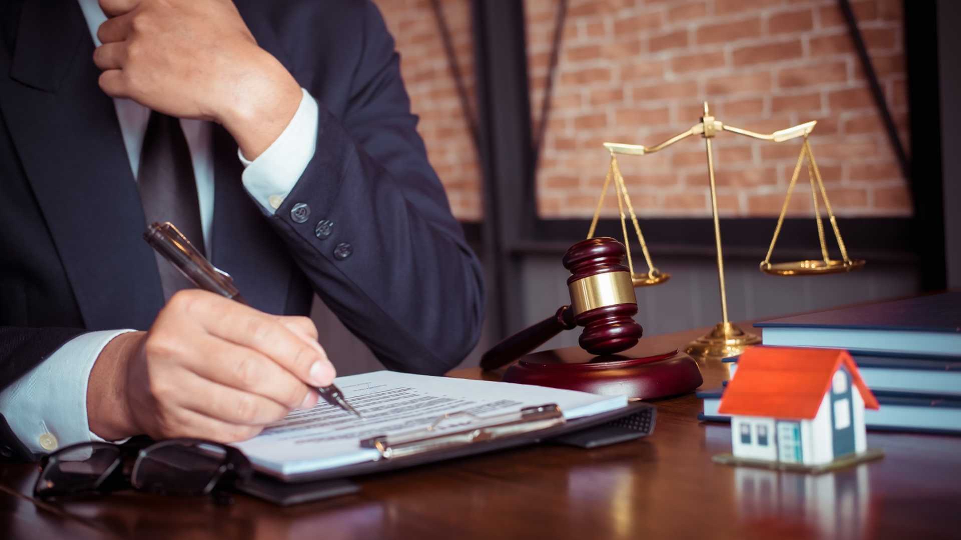person going over a document while sat at a desk with a gavel, a balance scale, and a model house on it